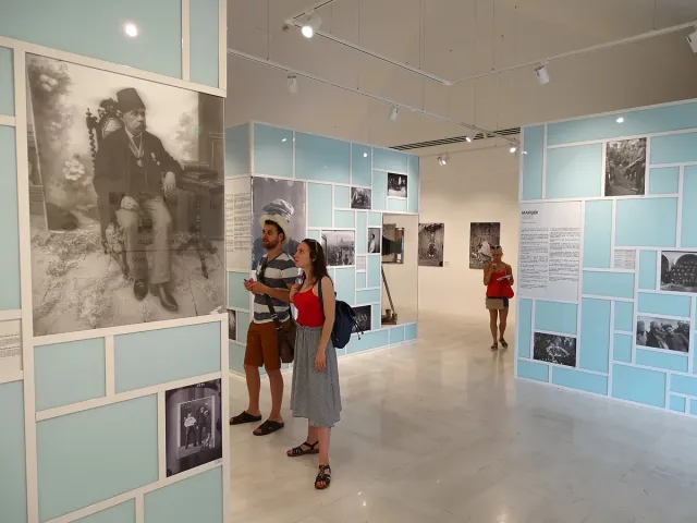 A bright gallery with historic photographs on pale blue walls, and visitors looking at an enlarged portrait