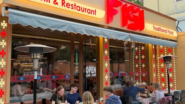 A front with an awning and red embroidery strips, lit letters and diners at the outdoor tables