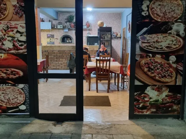 An entrance whose frames are covered in large pizza photographs, behind them a hall with a brick oven