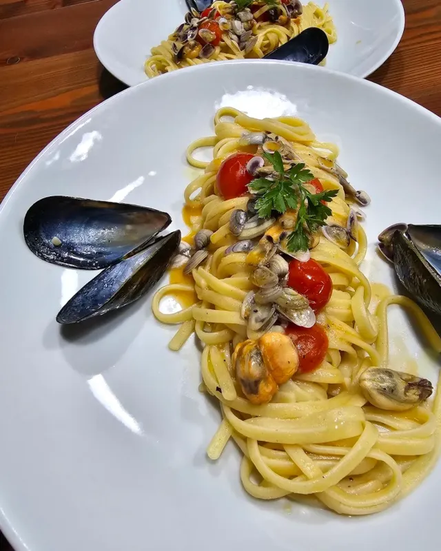 A plate of ribbon pasta with clams, mussels and cherry tomatoes and a parsley leaf