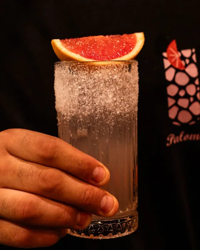 A hand holding a cocktail glass with a sugar rim and a red grapefruit wedge