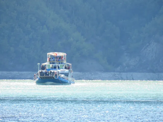 A blue passenger ferry crossing glittering water against a steep forested slope