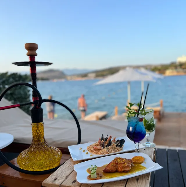 A hookah, a blue cocktail and seafood dishes on a table facing a calm bay