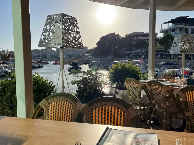 A table under a canopy facing a marina with moored boats and a low sun