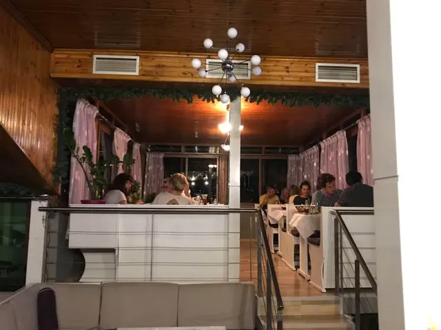 A room at night with a wooden ceiling, a globe chandelier, pink curtains and diners at tables