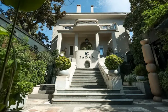 A white villa with columns, wide stone steps and shaped shrubs in pots on both sides