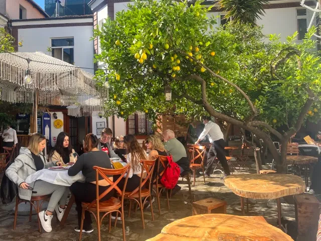 A courtyard with a lemon tree laden with fruit, diners around wooden tables and a woven umbrella