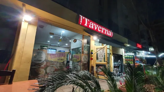 A glass front at night with a lit red sign and posters, and palm fronds in front