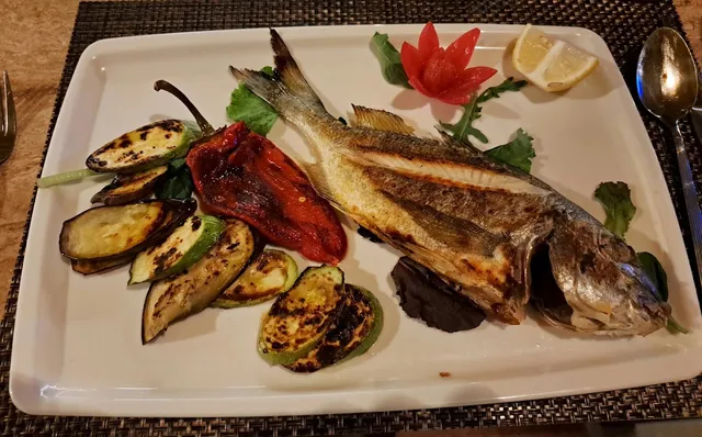 A whole grilled sea bream with eggplant, zucchini and roasted pepper on a rectangular plate