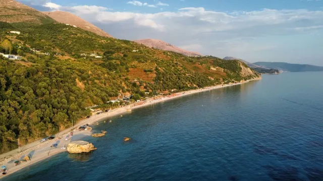An aerial shot of a curving bay with a pale beach, a green slope and a blue sea