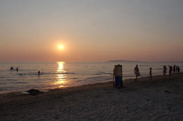 A sunset over the sea with a light trail on the water and silhouettes of bathers on the sand
