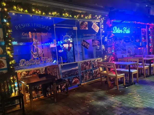 A front lit in blue with fish photographs and colored bulbs, and wooden benches outside at night