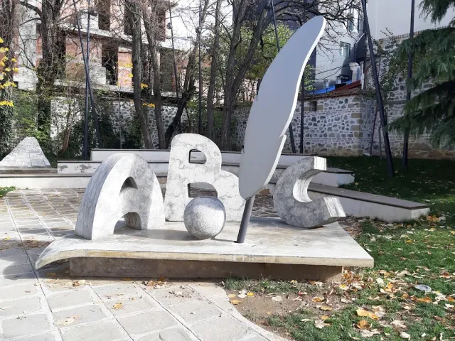 A stone sculpture shaped like letters and a writing quill in a paved yard with bare trees