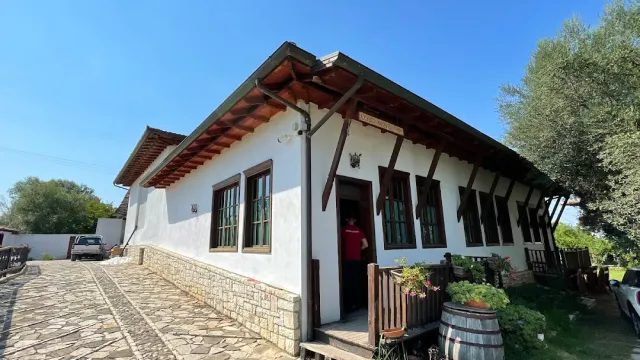 A low white building with wooden eaves, a stone yard and a wine barrel with flowers by the entrance