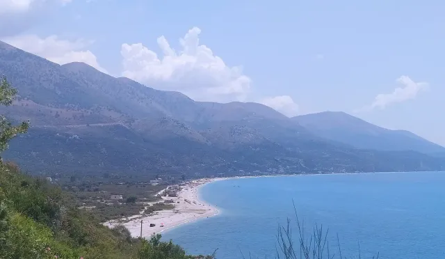 A long beach strip curving along the waterline beneath a bare mountain ridge