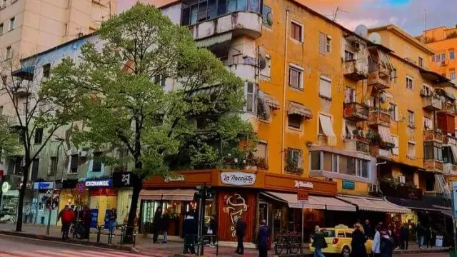 A street with colourful residential buildings, green trees and a corner shop with an awning