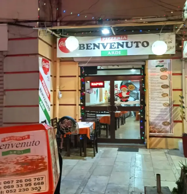 A lit entrance at night with a white sign, colored bulbs and tables with orange cloths inside