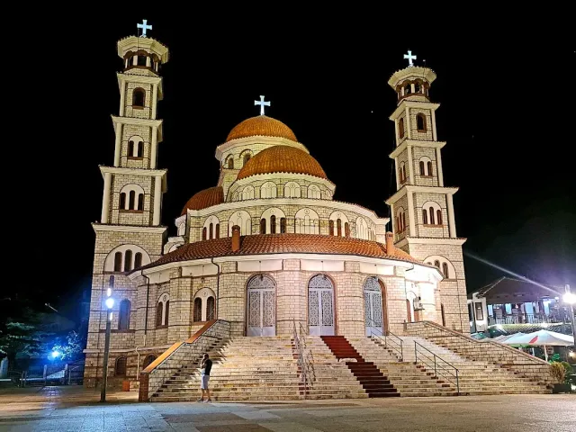 A church lit up at night with two bell towers, red domes and wide steps at the entrance