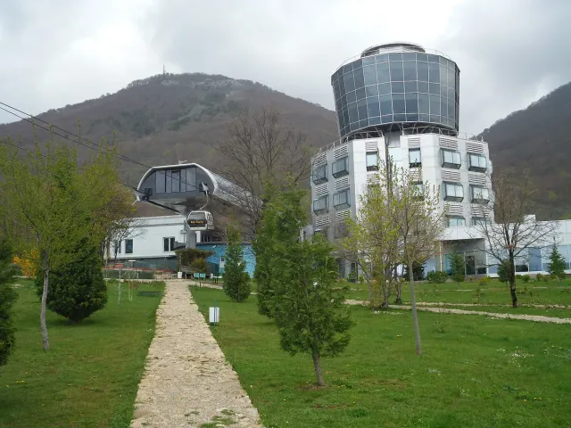A round glass clad building on a mountain slope beside a cable car station and a cabin on the line