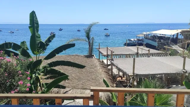 A view from a wooden balcony over thatched beach roofs, banana leaves and a blue sea with boats