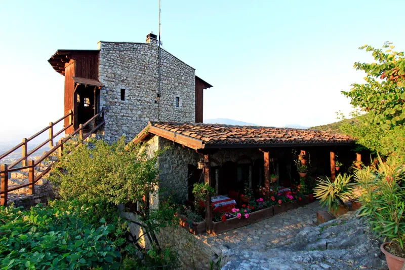 A stone tower with a wooden gallery above a covered terrace lined with red flowers