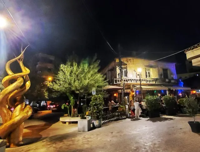 A street at night with a golden sculpture, lit trees and a busy venue terrace behind