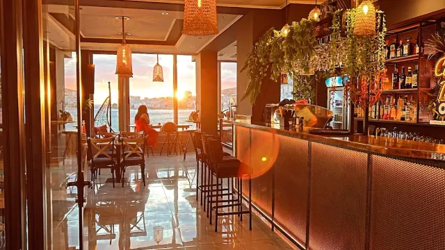 A long bar counter with stools and wicker lamps, and an orange sunset beyond the windows
