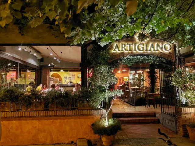 An entrance lit at night under foliage, an arched gate and olive trees in pots