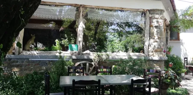 A shaded garden with tables and chairs, a stone wall, shade netting and an old cart wheel