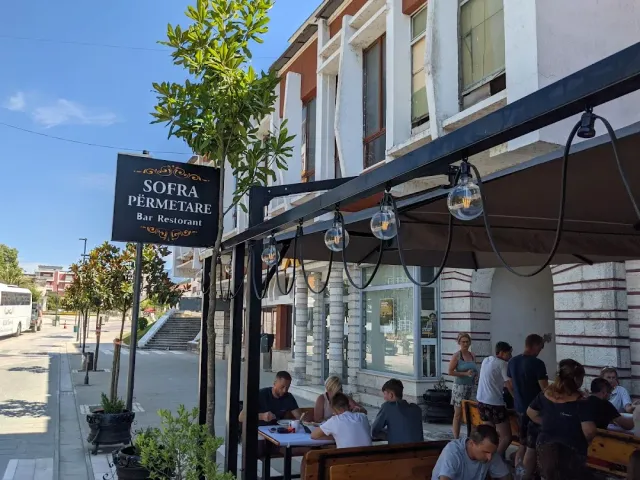 A hanging sign and bulbs above street tables with diners seated, facing an older building