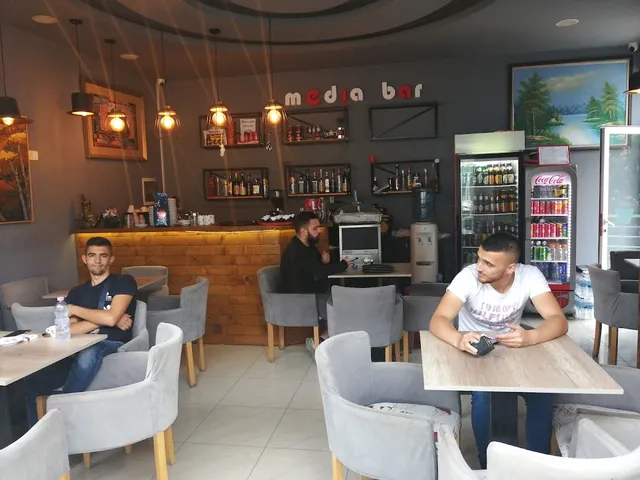 A bar space with gray armchairs, hanging lamps and bottle shelves on a dark wall