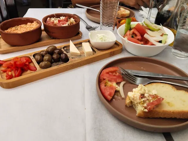 A table with clay bowls of spreads, a board of olives and cheeses and a bowl of vegetable salad