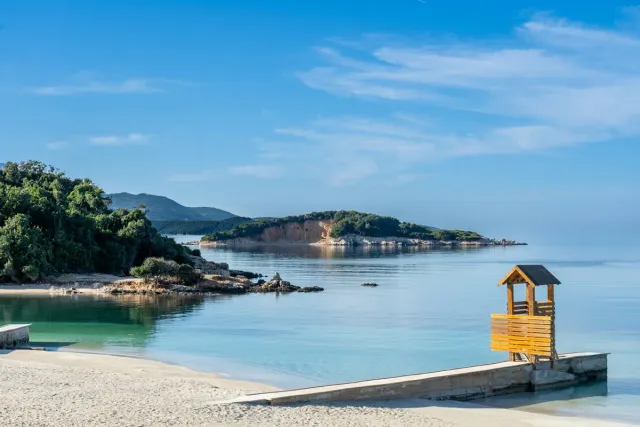 A calm bay of turquoise water with white sand, a yellow wooden tower and a green islet