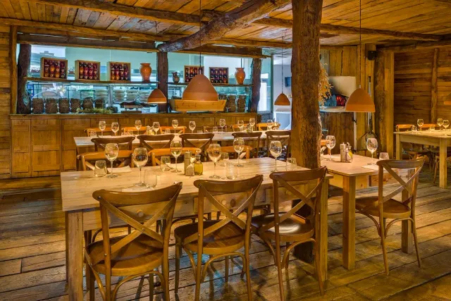 A rustic wooden hall with thick beams, hanging clay lamps and long tables