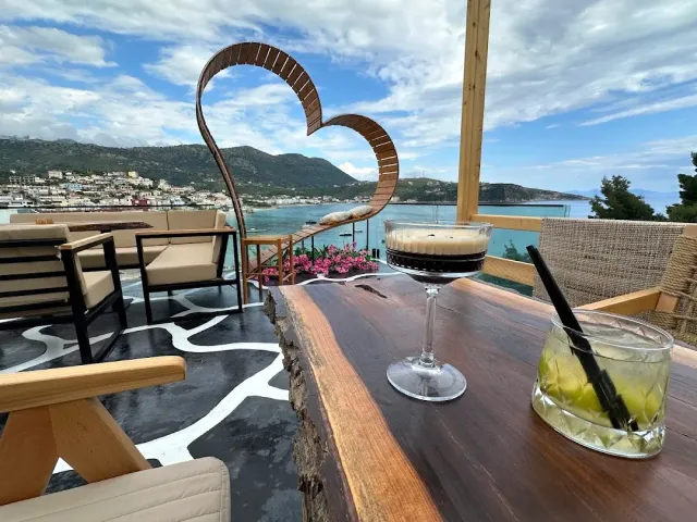 Two drinks on a wooden rooftop table, a heart shaped sculpture and a bay and hills behind