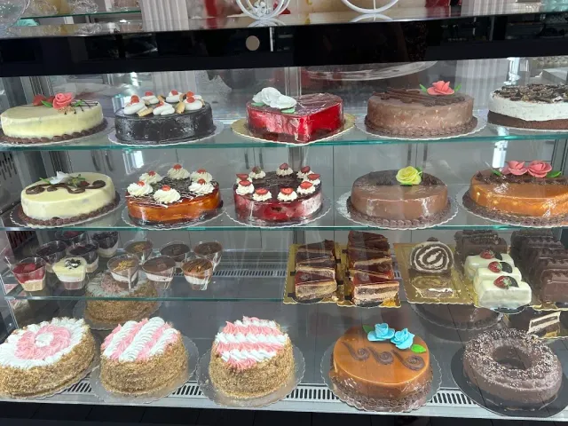 A glass display case with whole cakes decorated with cream and sugar roses on three shelves