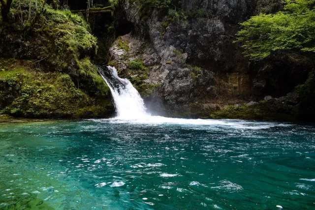 A small waterfall pouring into a clear turquoise pool between rock walls and trees