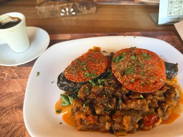 A plate with baked eggplants under tomato slices beside a vegetable stew, and a cup of black coffee