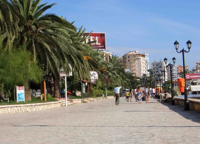 A wide paved promenade between tall palms and street lamps, with pedestrians and holiday buildings