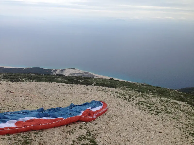 A paraglider wing spread on a slope above the coastline