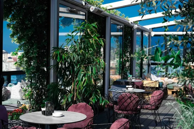 A glazed terrace with pink velvet armchairs, marble tables and lush greenery