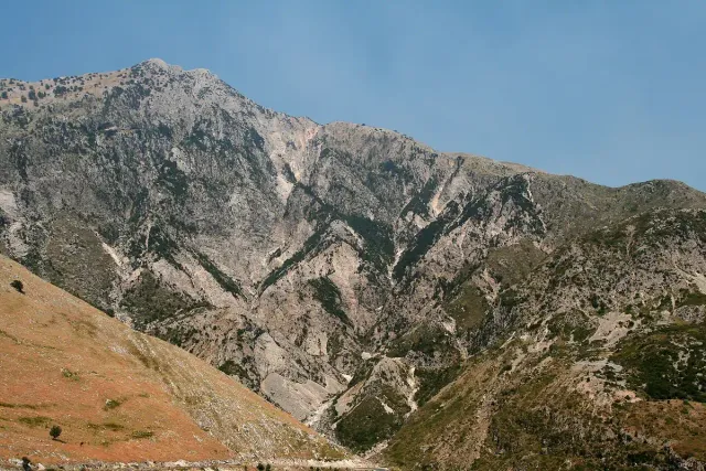 A steep rocky mountain slope with deep gullies against a blue sky