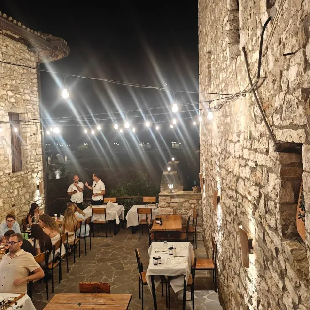 A stone alley at night with a string of bulbs, tables in white cloths and diners seated