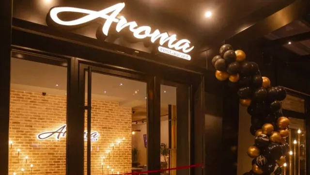 An entrance at night with a lit script sign, an arch of black and gold balloons and lit candles