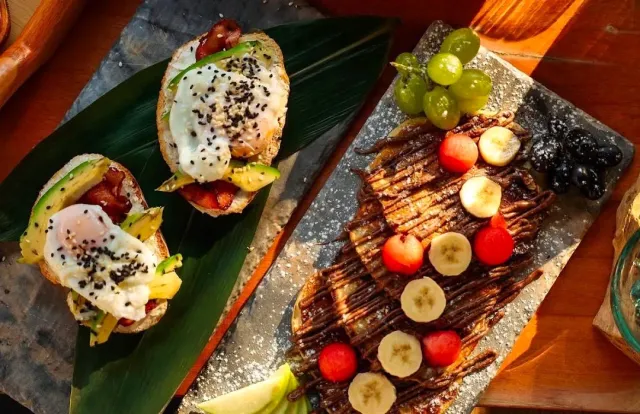 An overhead view of two sandwiches with egg and avocado beside a crepe with banana and strawberries