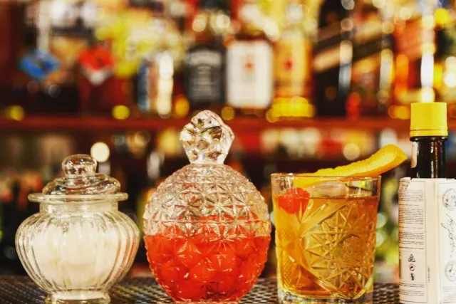 Crystal jars and a cocktail glass with an orange peel in front of a blurred shelf of bottles