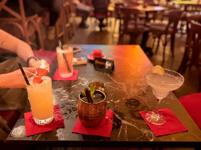 Three cocktails on a dark marble table, with red napkins and a copper mug