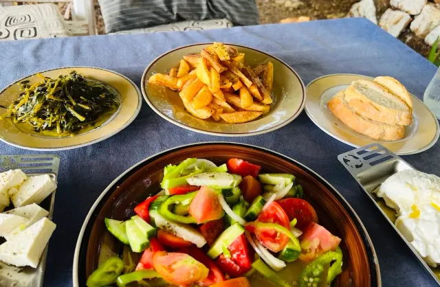 A table with a bowl of vegetable salad, a plate of fries, cooked greens and slices of bread