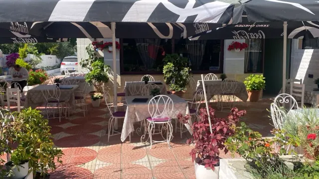 A tiled courtyard with striped parasols, white metal chairs and flower pots