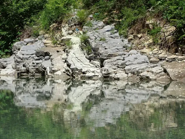 A white limestone bank reflected in still green water between wooded slopes